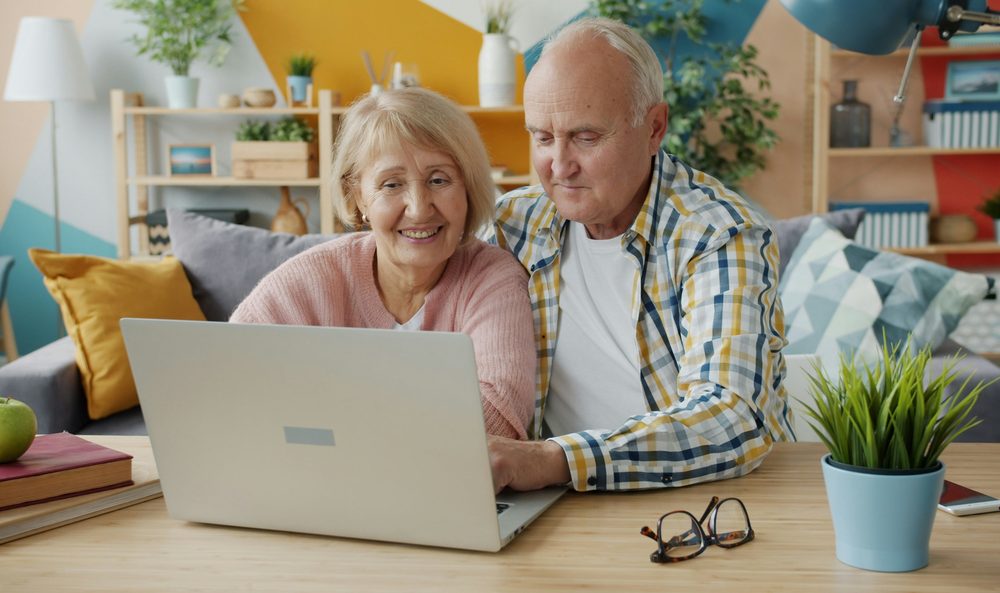 A smiling senior couple on a couch looking at a laptop together